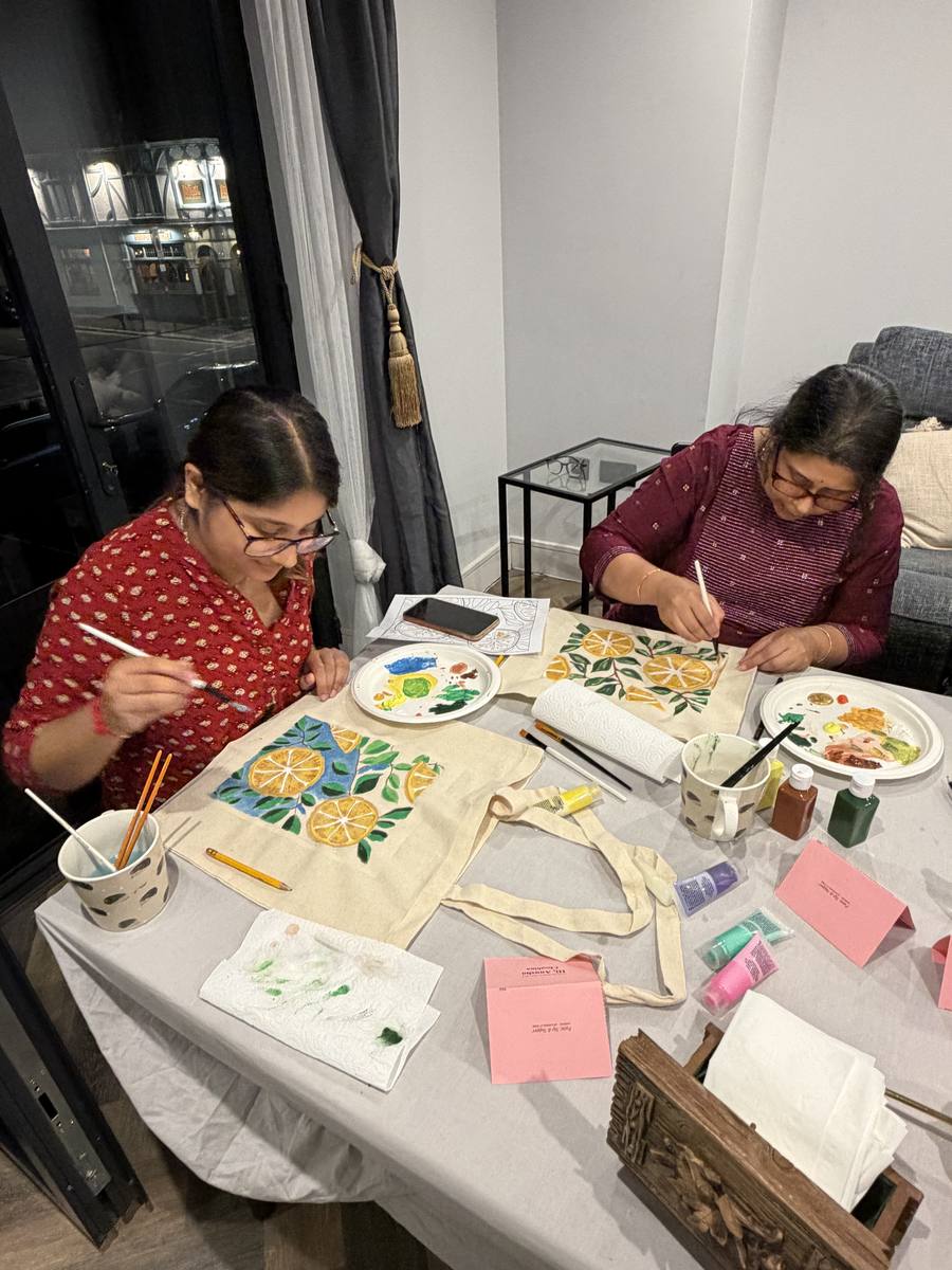 Two guests painting citrus designs onto tote bags at the supper table