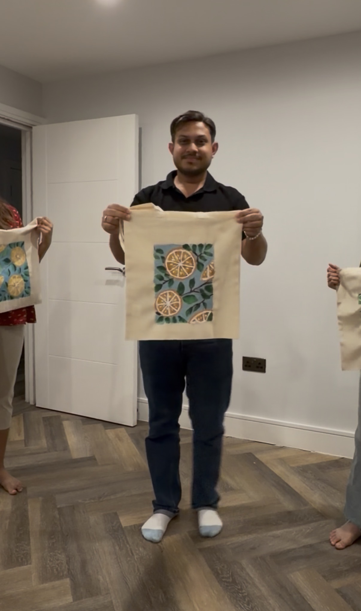 A guest holding up his finished citrus-painted tote bag, with other guests' totes visible either side